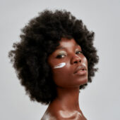 Beauty portrait of young naked african american woman with afro hair looking at camera while posing with cream applied on her face isolated over gray background Beauty portrait of young naked african american woman with afro hair looking at camera while posing with cream applied on her face isolated over gray background